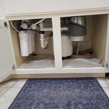 Under-sink plumbing Sink cabinet showing drain piping, a filter unit and garbage disposal