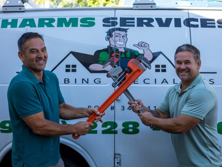 The Harms Services owners holding pipe wrenches beside their branded company van