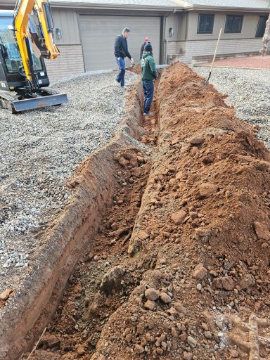 Exterior plumbing excavation Long excavated trench beside a paved area