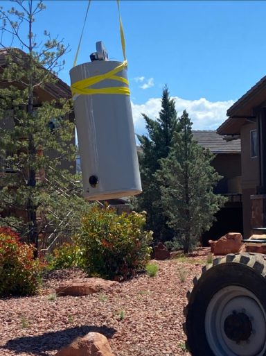 Water heater removal Large cylindrical water heater being lifted outside a home