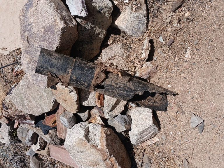 Harms Services pipe project photo Damaged black pipe with roots around its broken section, resting on rocks.